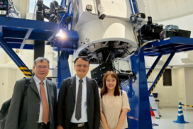 Three visitors pose in front of a large research telescope during a laboratory tour